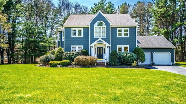colonial home featuring roof with shingles, an attached garage, a front yard, and aphalt driveway