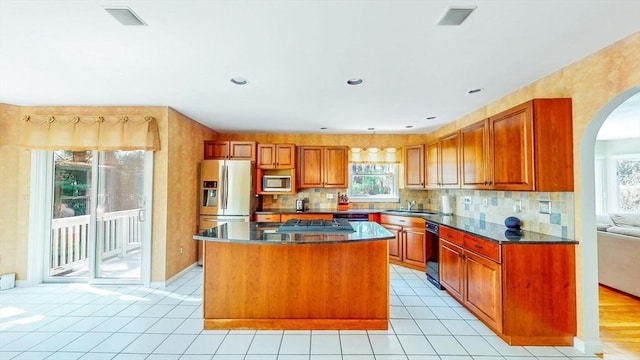 kitchen featuring a sink, arched walkways, brown cabinetry, a center island, and stainless steel appliances
