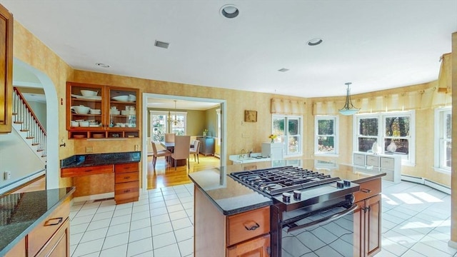 kitchen with visible vents, a kitchen island, stainless steel range with gas stovetop, a baseboard radiator, and light tile patterned floors