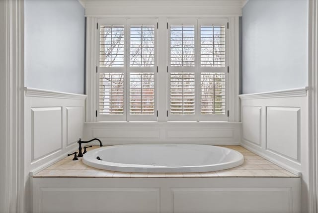 bathroom with a garden tub, a decorative wall, and a wainscoted wall