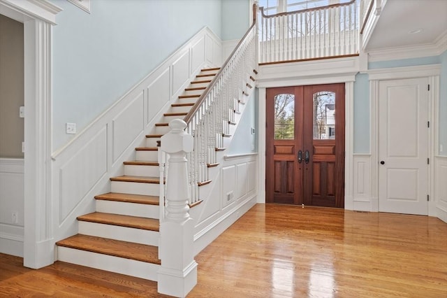 foyer entrance with wood finished floors, stairway, french doors, crown molding, and a decorative wall