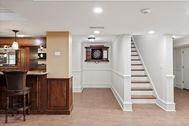 bar with visible vents, crown molding, stairway, a wainscoted wall, and light wood-style flooring