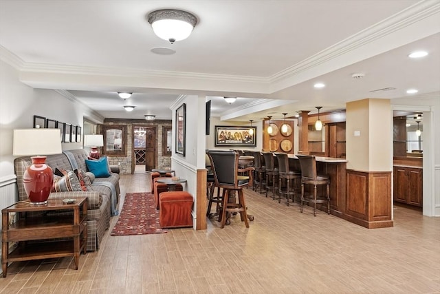 living area featuring crown molding, light wood-style floors, indoor bar, and wainscoting