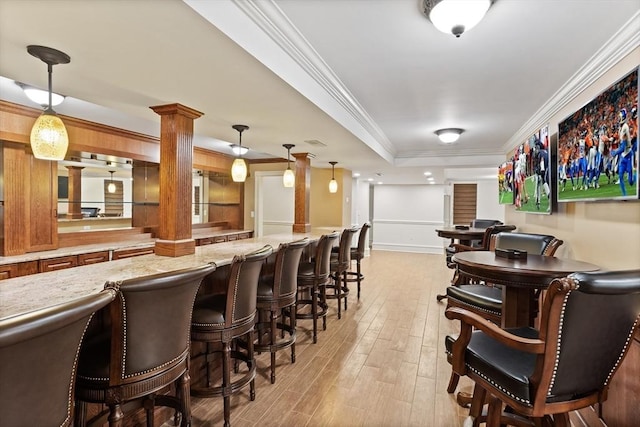 bar with light wood finished floors, decorative columns, hanging light fixtures, crown molding, and a raised ceiling