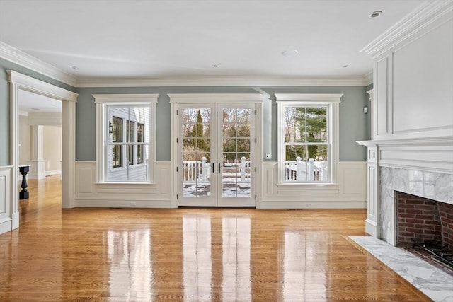 doorway featuring a wainscoted wall, a premium fireplace, light wood-style floors, french doors, and crown molding