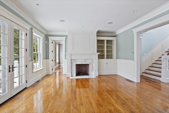 unfurnished living room with a high end fireplace, stairway, light wood finished floors, and a wainscoted wall