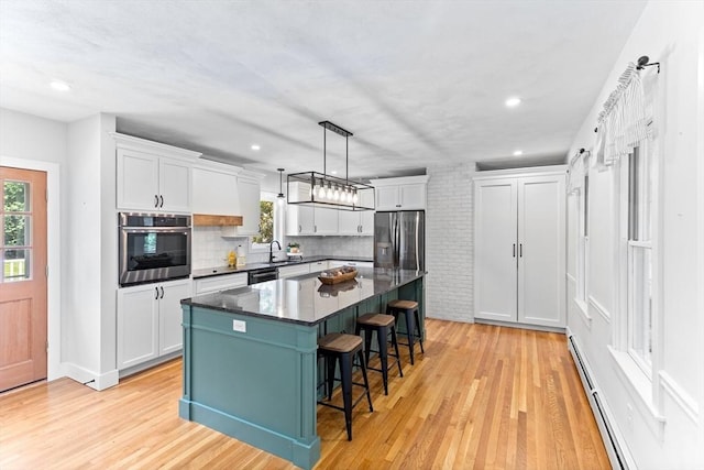 100 Gilbert St, Mansfield, MA 02048 - kitchen featuring appliances with stainless steel finishes, white cabinets, a breakfast bar area, a center island, and light wood-style flooring