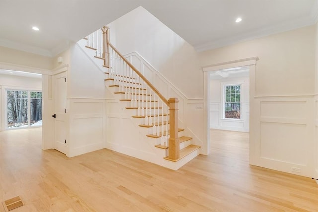 stairway featuring crown molding, a healthy amount of sunlight, a decorative wall, and wood finished floors