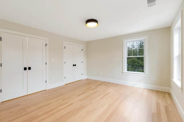 unfurnished bedroom with light wood finished floors, baseboards, and multiple closets