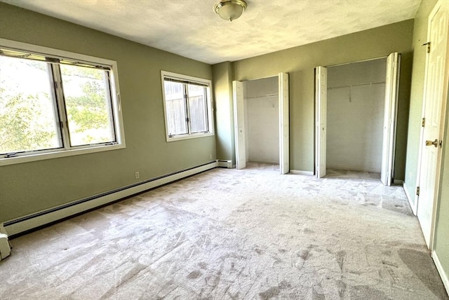 unfurnished bedroom featuring baseboard heating, multiple closets, carpet flooring, and baseboards