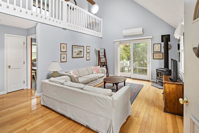 living room with an AC wall unit, high vaulted ceiling, a wood stove, and light hardwood / wood-style flooring