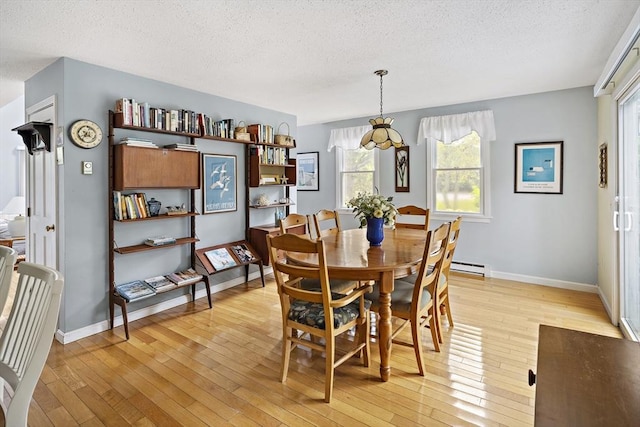 dining area with a textured ceiling, light wood-type flooring, plenty of natural light, a baseboard radiator, and baseboards