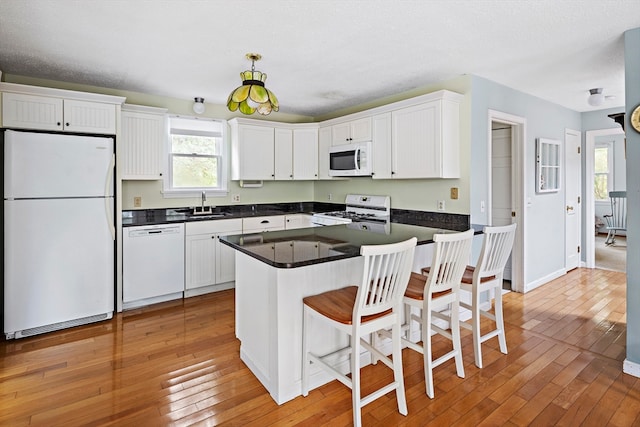 kitchen with white appliances, a kitchen bar, hardwood / wood-style floors, and white cabinets