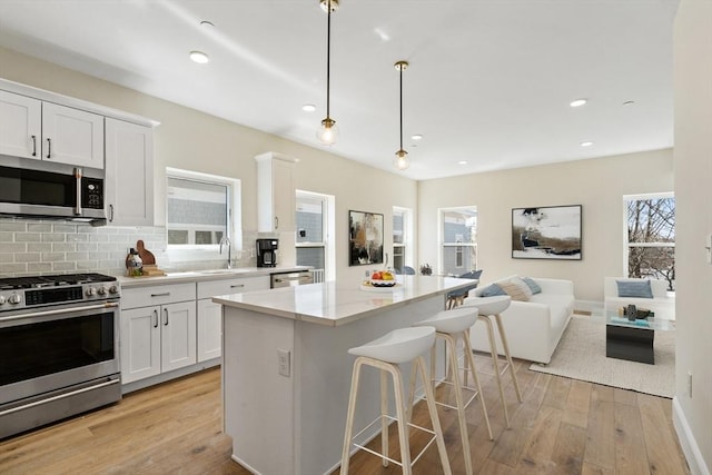 kitchen featuring white cabinets, hanging light fixtures, decorative backsplash, light wood-type flooring, and appliances with stainless steel finishes