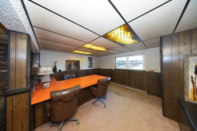 office area featuring a baseboard radiator, a drop ceiling, wood walls, built in desk, and carpet