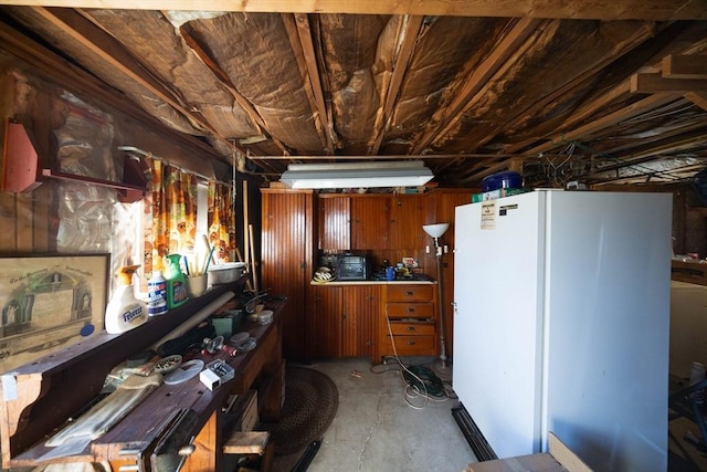 kitchen featuring unfinished concrete floors, brown cabinetry, and freestanding refrigerator