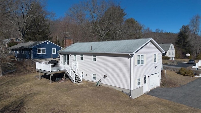 back of property with a garage, driveway, a chimney, a deck, and a yard