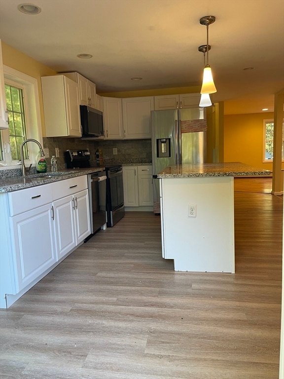 kitchen featuring tasteful backsplash, white cabinetry, light hardwood / wood-style flooring, appliances with stainless steel finishes, and decorative light fixtures