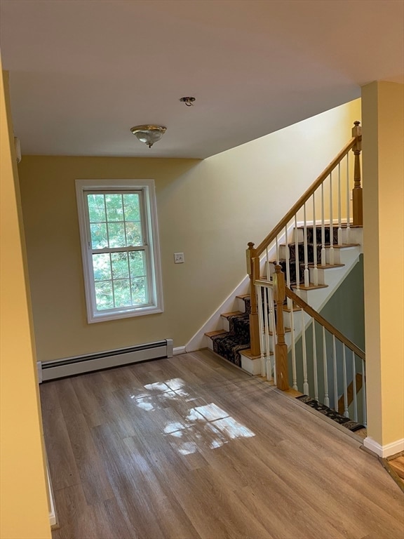 stairs featuring wood-type flooring and a baseboard heating unit