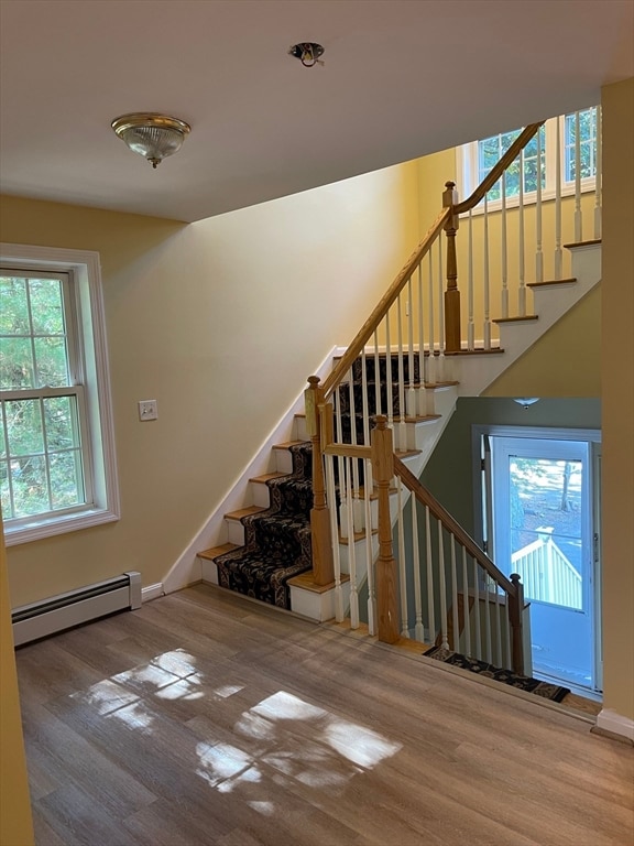 stairs featuring baseboard heating, hardwood / wood-style flooring, and a healthy amount of sunlight