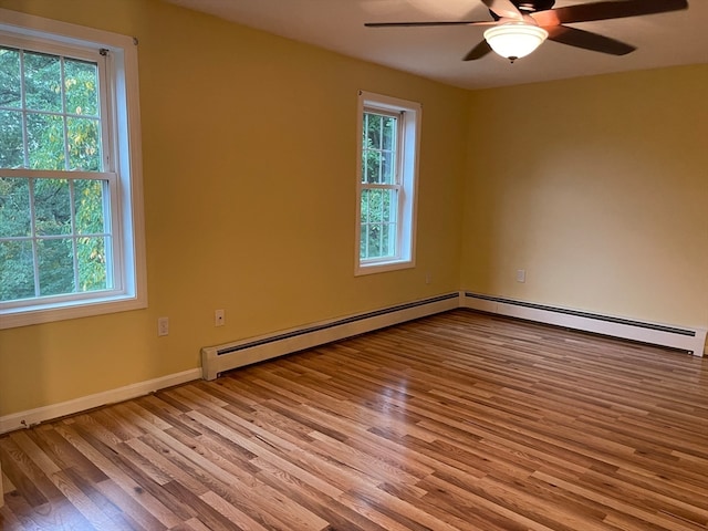 empty room with a healthy amount of sunlight, a baseboard heating unit, and light hardwood / wood-style floors