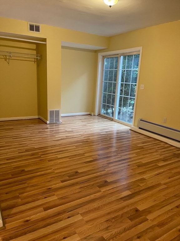 unfurnished bedroom with a closet, a baseboard heating unit, and light hardwood / wood-style flooring