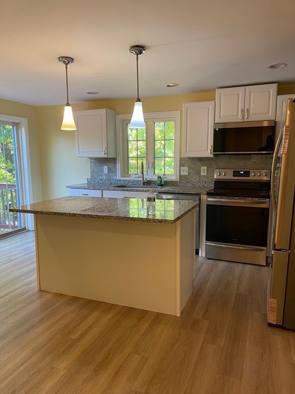 kitchen featuring tasteful backsplash, light stone counters, stainless steel appliances, hanging light fixtures, and white cabinetry