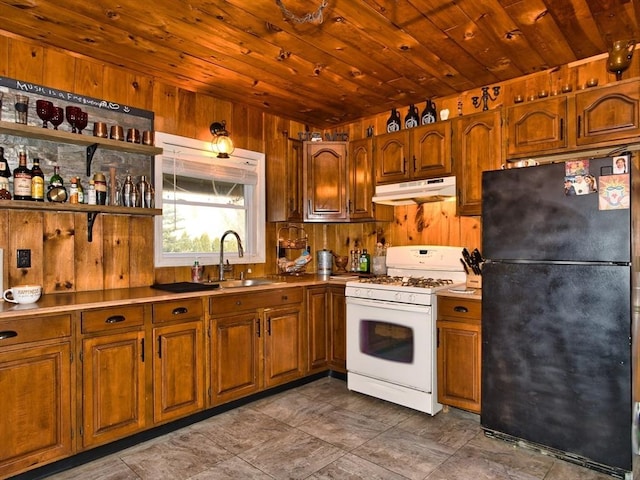 kitchen with black fridge, white gas range, sink, and wooden walls