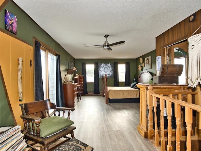 bedroom with a textured ceiling, light hardwood / wood-style flooring, ceiling fan, and wooden walls