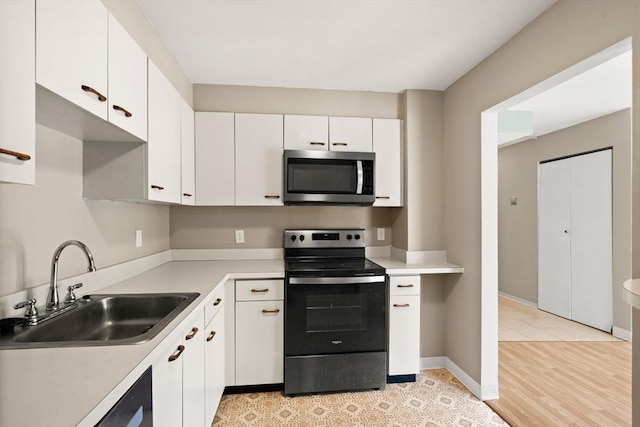 kitchen with light wood-type flooring, range with electric stovetop, white cabinetry, and sink