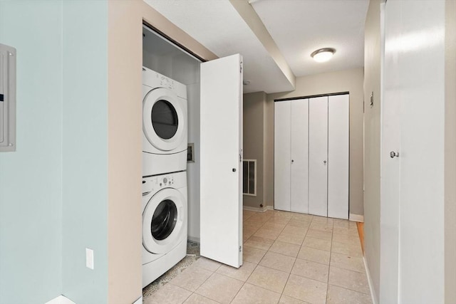 laundry area with light tile patterned floors and stacked washing maching and dryer