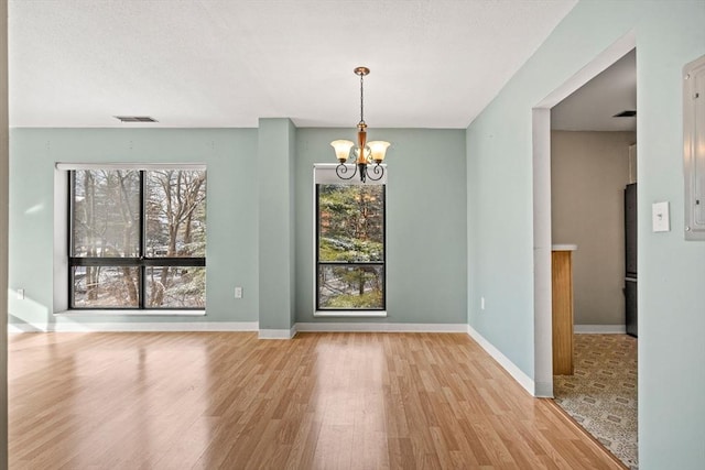 unfurnished dining area with a notable chandelier, a wealth of natural light, and light hardwood / wood-style flooring