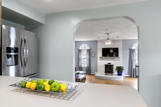 kitchen featuring arched walkways, stainless steel refrigerator with ice dispenser, wood finished floors, and a wood stove