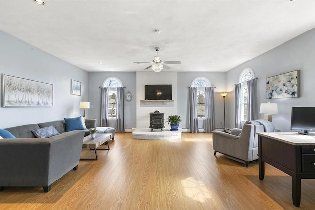 living area featuring a ceiling fan, a wood stove, and light wood-style floors