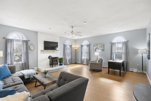 living room with baseboard heating, a wood stove, baseboards, and wood finished floors