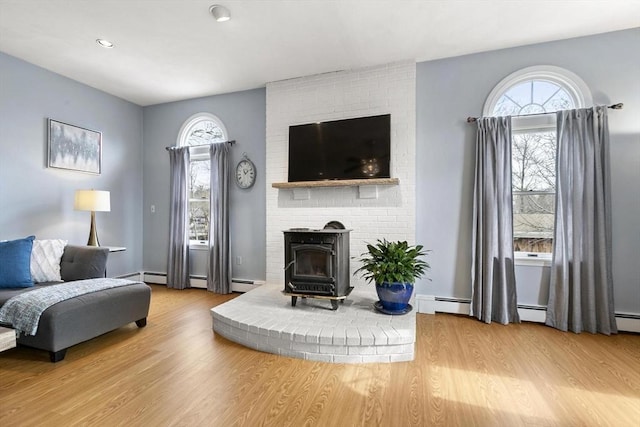 living room featuring a baseboard heating unit, wood finished floors, a wood stove, and a healthy amount of sunlight