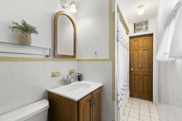 full bathroom featuring toilet, a wainscoted wall, tile patterned floors, vanity, and tile walls