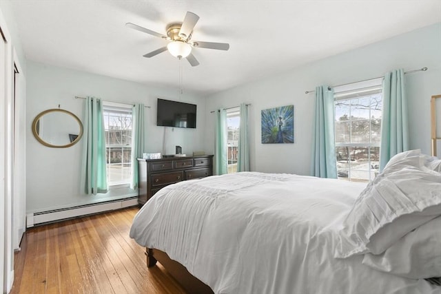 bedroom with a baseboard heating unit, hardwood / wood-style floors, and a ceiling fan