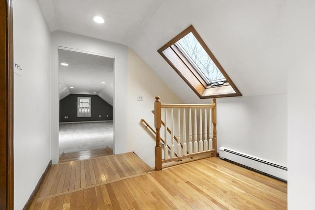 additional living space featuring vaulted ceiling with skylight, wood-type flooring, and baseboard heating