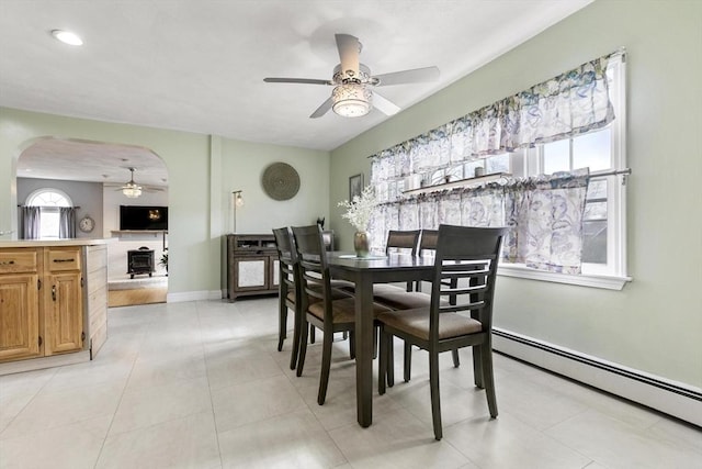 dining area featuring arched walkways, ceiling fan, light tile patterned floors, a baseboard radiator, and baseboards