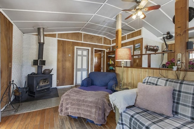 living area with a ceiling fan, a wood stove, wood walls, wood-type flooring, and lofted ceiling