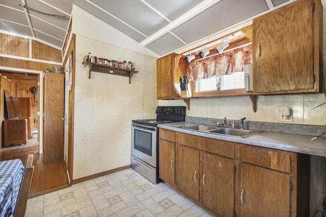 kitchen featuring brown cabinetry, electric range, baseboards, a sink, and vaulted ceiling