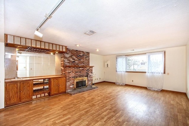 unfurnished living room featuring a brick fireplace, a textured ceiling, and light hardwood / wood-style floors