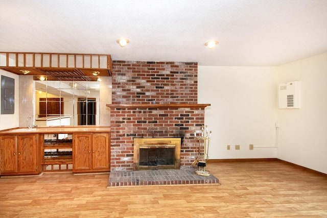 unfurnished living room with a brick fireplace, electric panel, light hardwood / wood-style floors, and sink