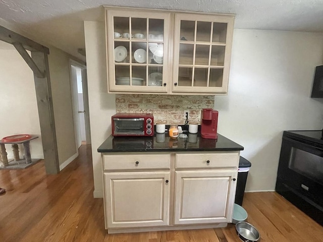 bar featuring backsplash, black range with electric stovetop, and light wood-type flooring