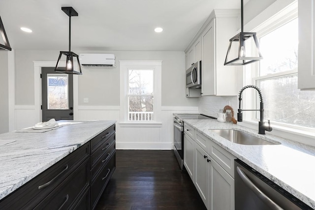 kitchen featuring a wall mounted air conditioner, sink, appliances with stainless steel finishes, decorative light fixtures, and white cabinetry