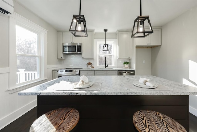 kitchen featuring sink, tasteful backsplash, a wall unit AC, decorative light fixtures, and appliances with stainless steel finishes