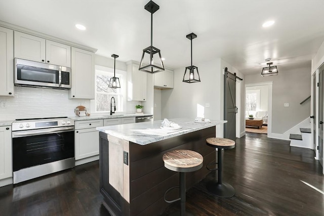 kitchen featuring white cabinets, hanging light fixtures, a barn door, appliances with stainless steel finishes, and a kitchen island