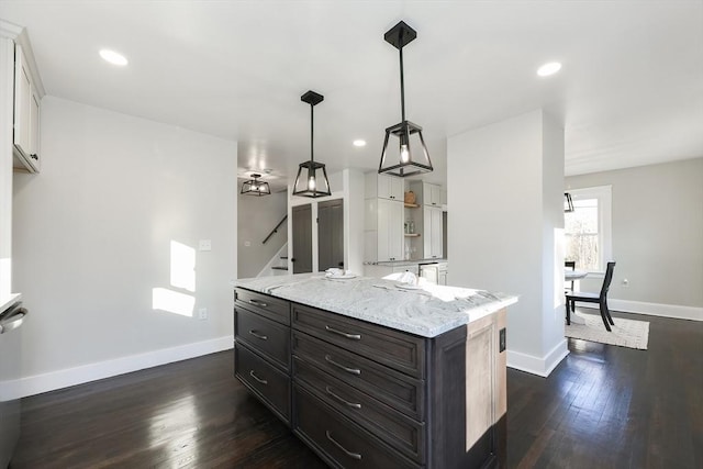 kitchen with light stone counters, dark wood-type flooring, white cabinets, a center island, and hanging light fixtures