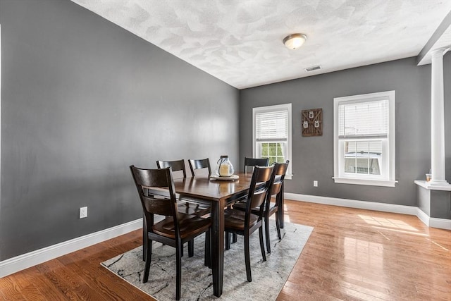 dining area featuring visible vents, baseboards, light wood-style flooring, and ornate columns